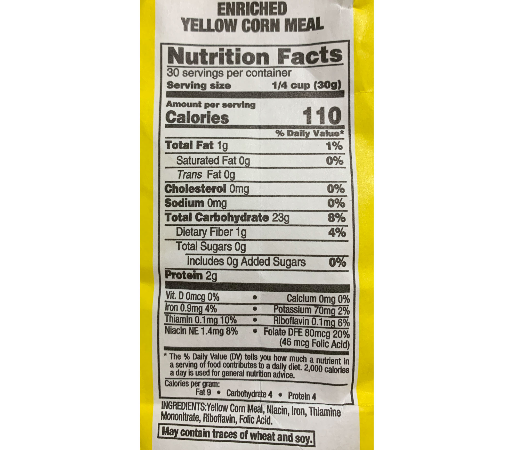 Photograph of a nutritional label from a package of corn meal, U.S.A. The top of the label says "enriched yellow corn meal" in all-caps. Beneath that is a box labeled "Nutrition Facts" with nutritional information. Below the box is a list of ingredients. The ingredients are yellow corn meal, niacin, iron, thiamine mononitrate, riboflavin, folic acid. Below that is a small box that says "May contain traces of wheat and soy."