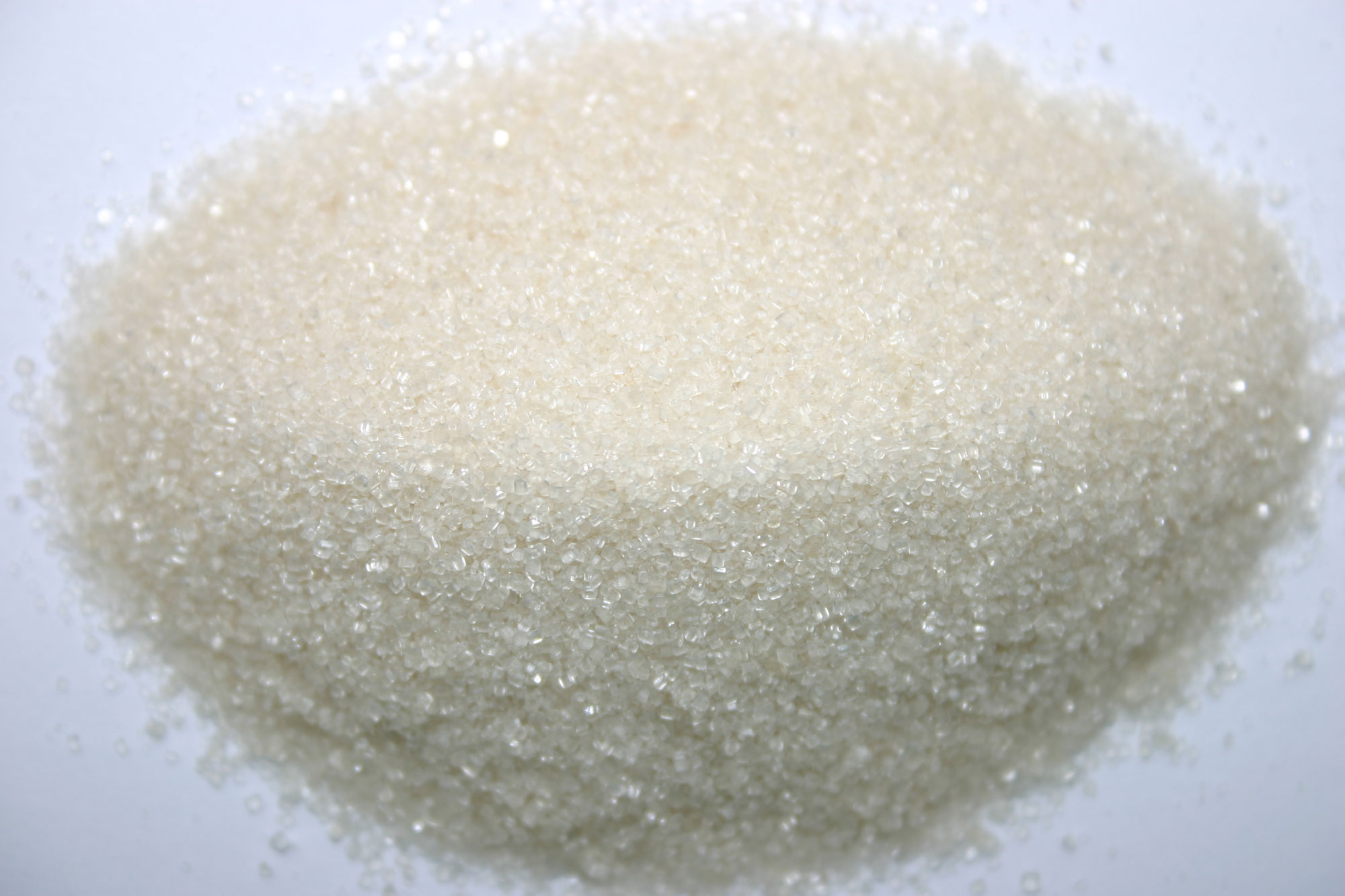 Photograph of a pile of white sugar. The photo shows white crystalline sugar on a white background.