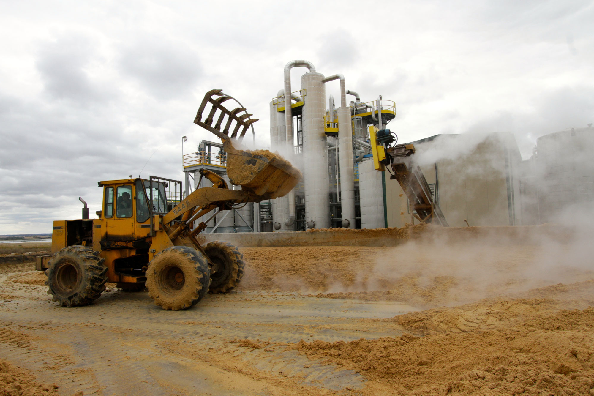 Photograph of a front-end loader moving distillers grains in front of an ethanol plant. 