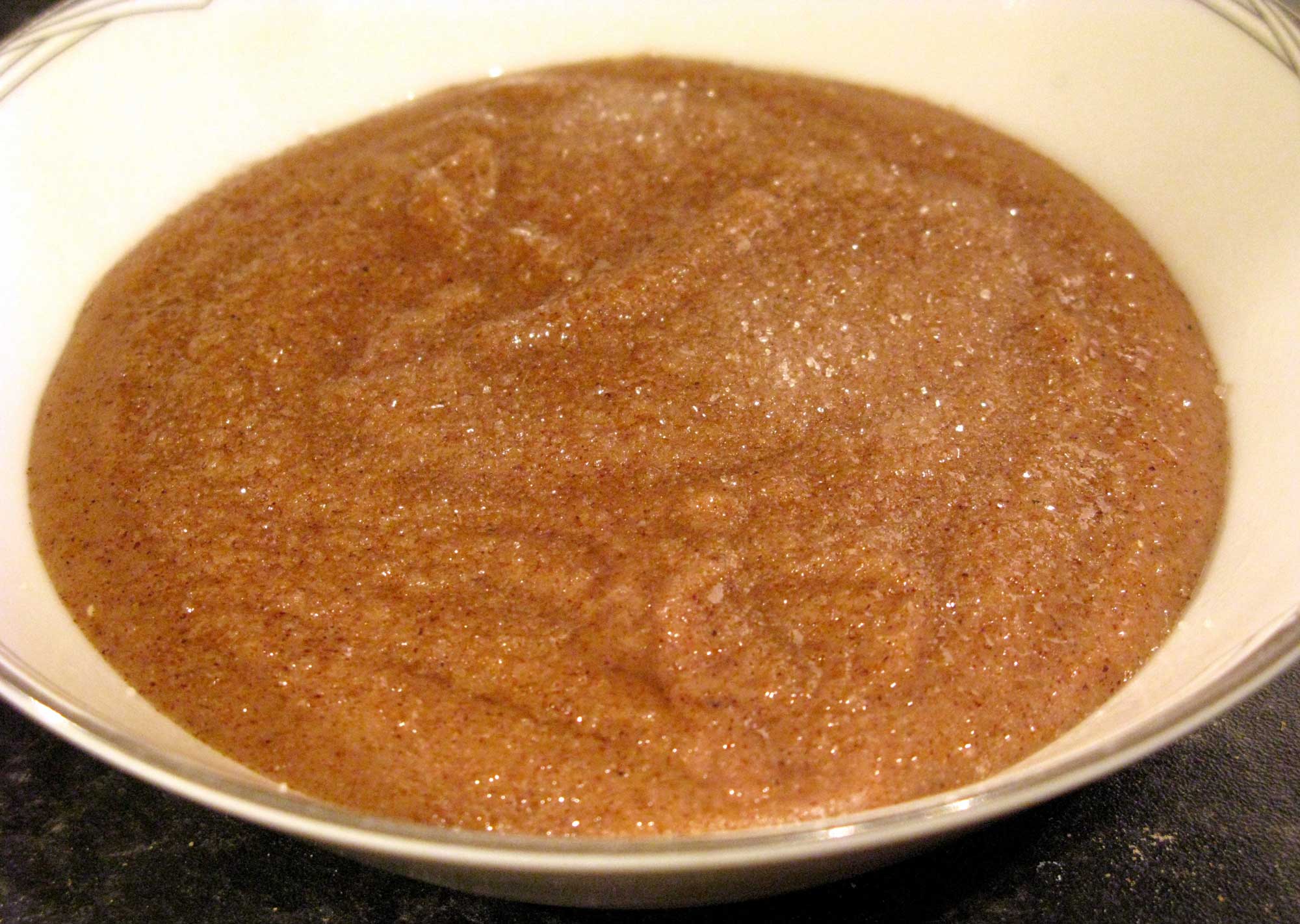 Photograph of sorghum porridge. The photo shows a thick, granular, brown porridge in an off-white bowl.