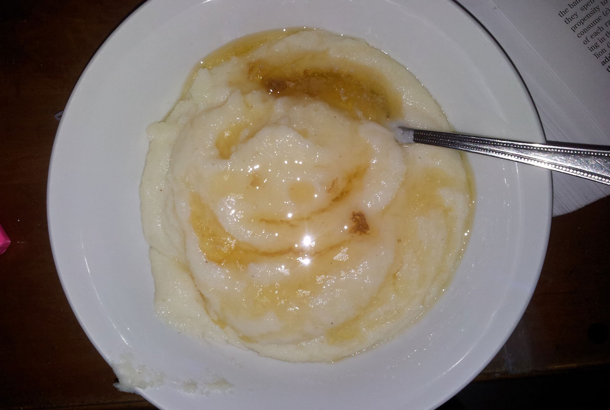 Photograph of a bowl of maize porridge from South Africa. The photo shows a white bowl filled with porridge that appears to have syrup on it. A spoon is resting in the porridge.