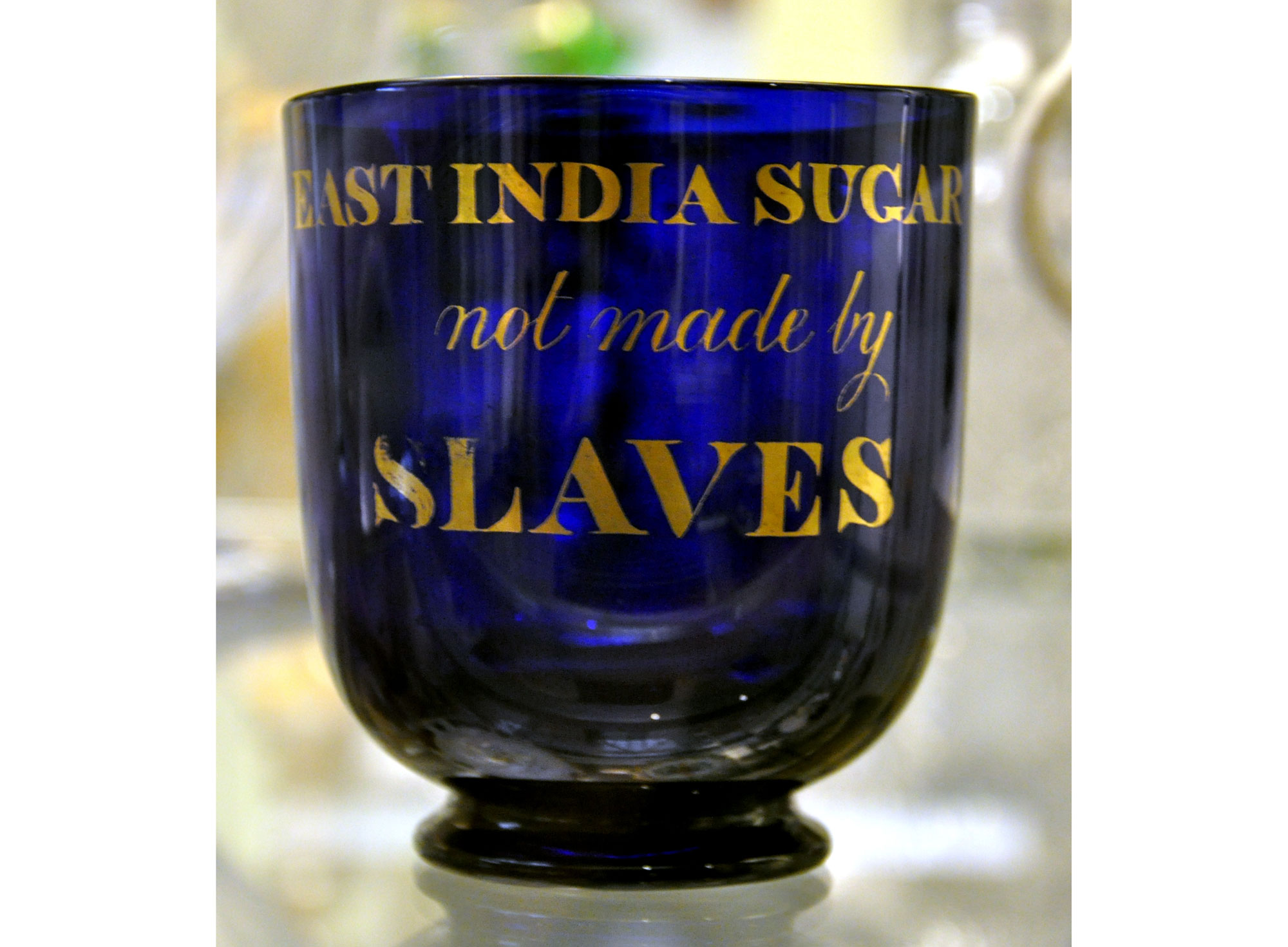 Photograph of a dark blue glass sugarbowl. The sugarbowl has gold lettering on it that says "East India Sugar not made by Slaves."