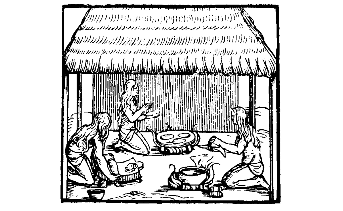 Black and white engraving of Taino women making cassava bread. The engraving shows three women in an open-sided hut. One woman appears to be rolling dough, one appears to be cooking patties on a flat rock or pan over a fire, and one shows a women in front of a kettle that has been placed on a fire.