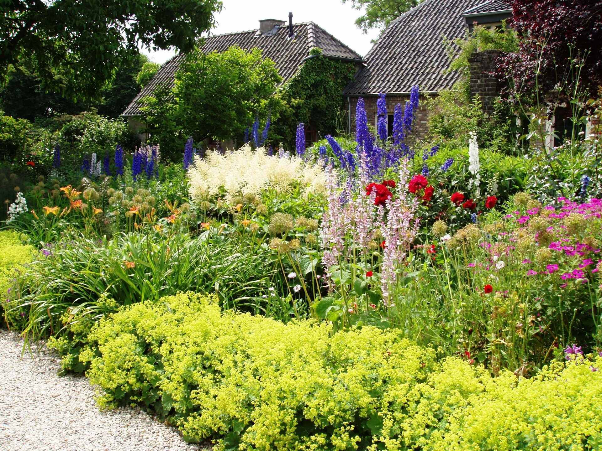 Photograph of a flower garden. The photo shows a well maintained garden bordering a gravel path. A house is partially obscured in the background.