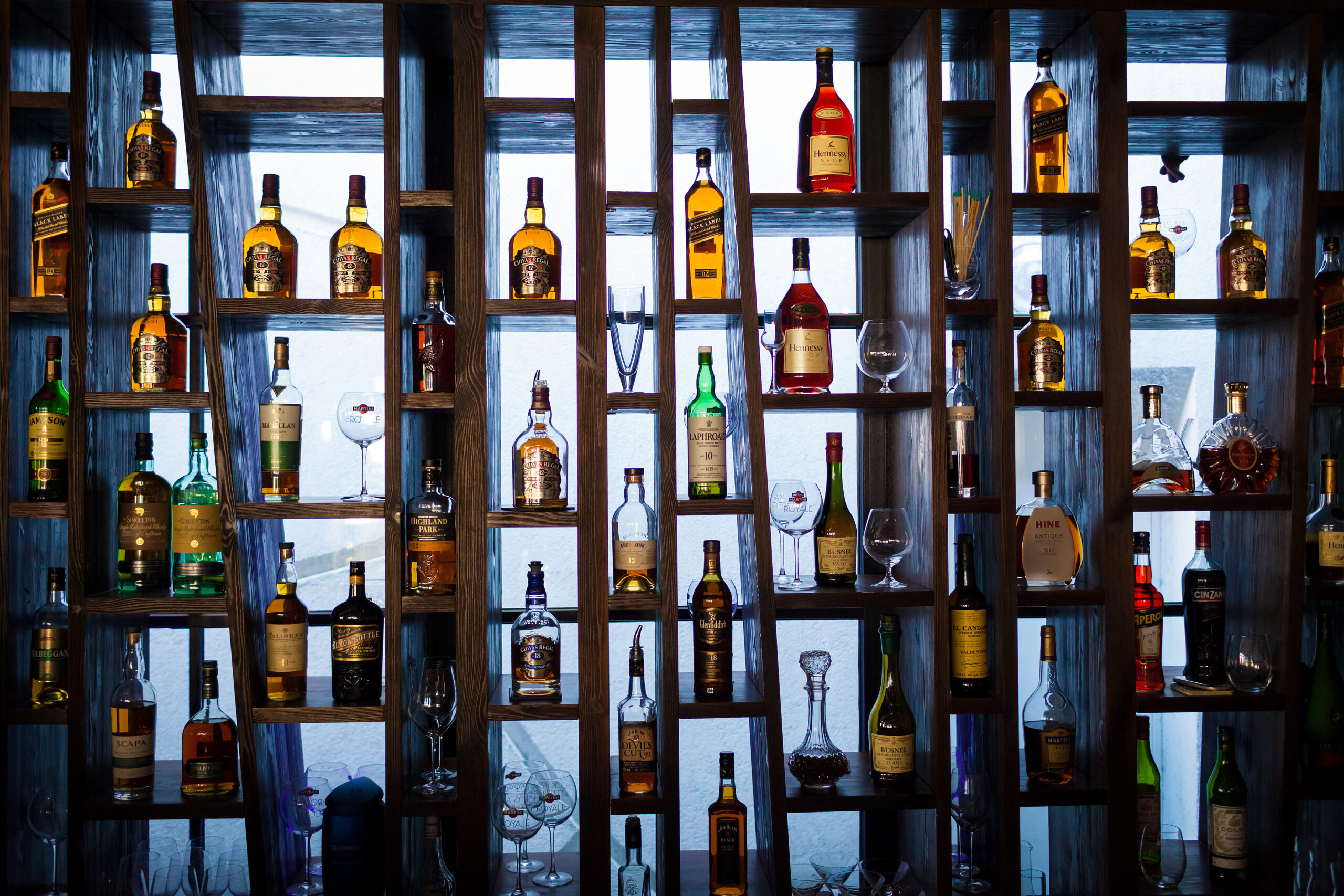 Photograph of shelves with bottles of alcoholic beverages and wine glasses on them.