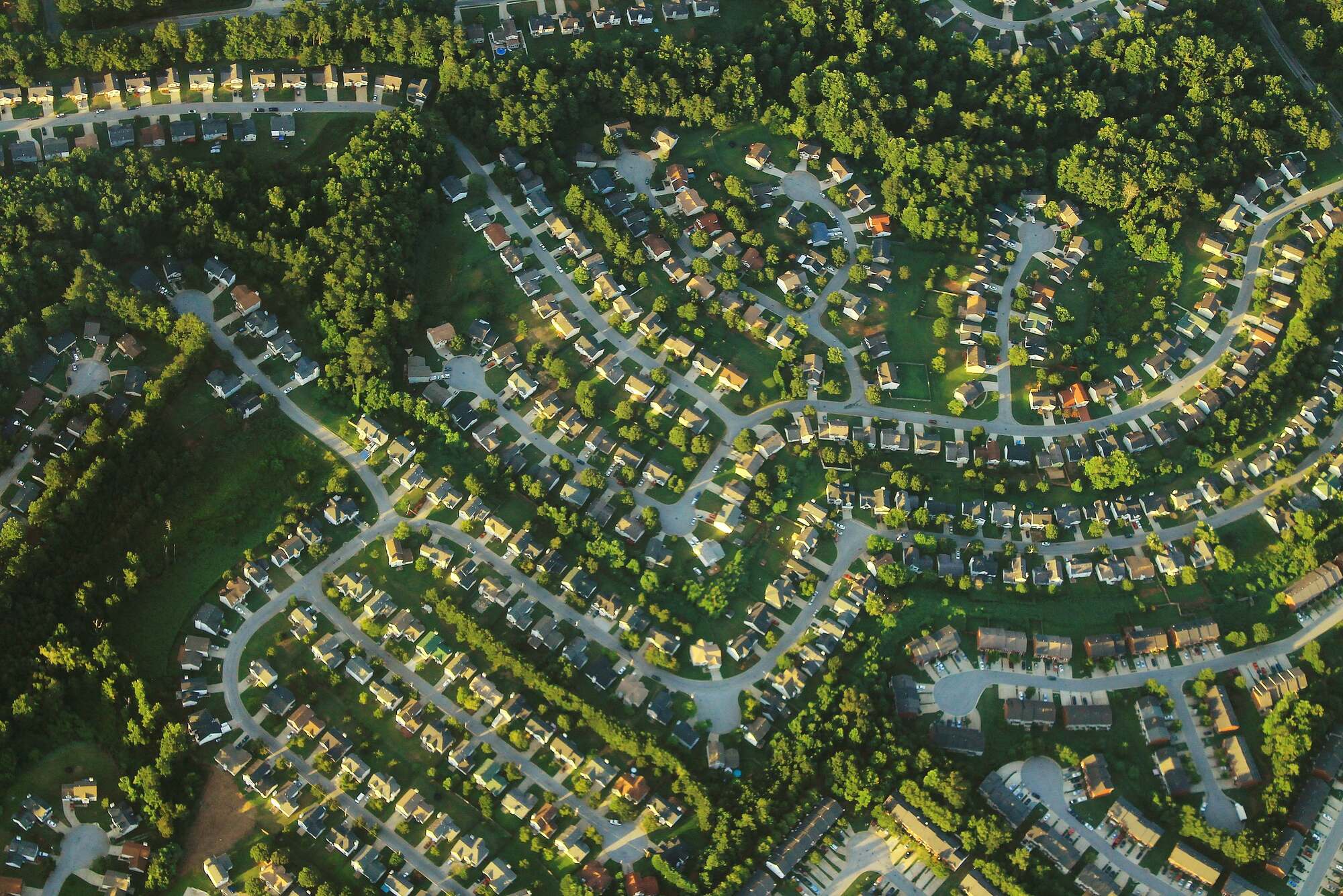 Aerial photograph showing a residential neighborhood near Atlanta with curving streets and closely spaced houses. Green lawns and trees are growing around the houses.