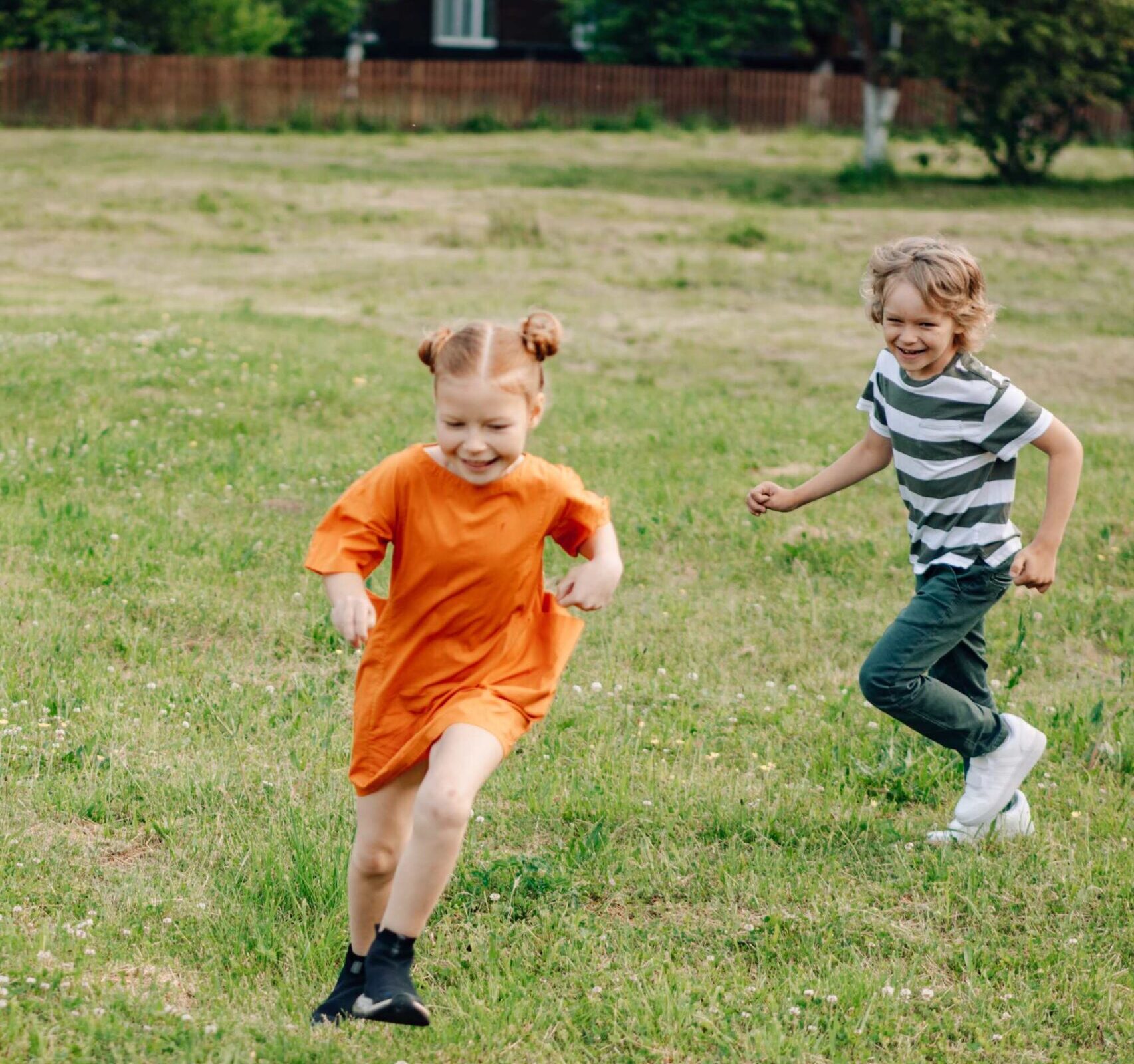 Photograph of a young girl and boy chasing each other in the grass.