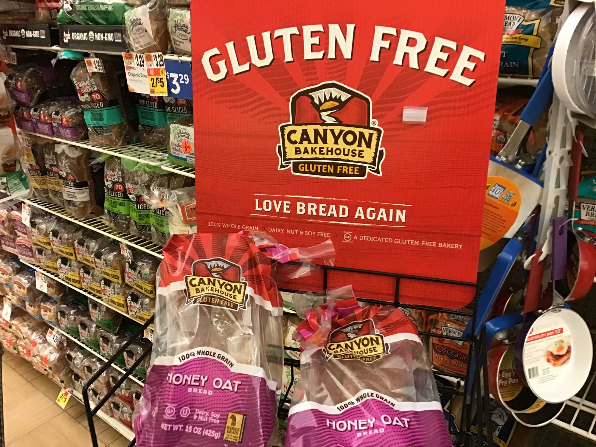 Photograph of a display of gluten free bread at a grocery store. A red sign at the top of the display says "Gluten Free" in large white letters. Two loaves of prepackaged and sliced bread also have labels reading "gluten free."