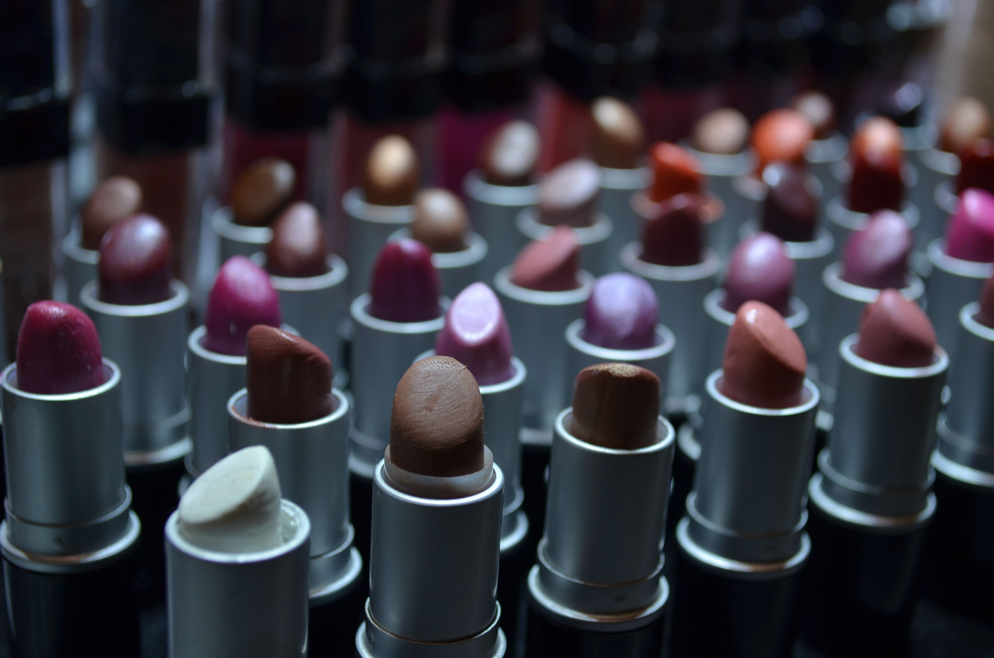 Photograph of tubes of lipstick with their caps off. The lipsticks are different colors, including white, brown, and shades of red, pink, and purple.