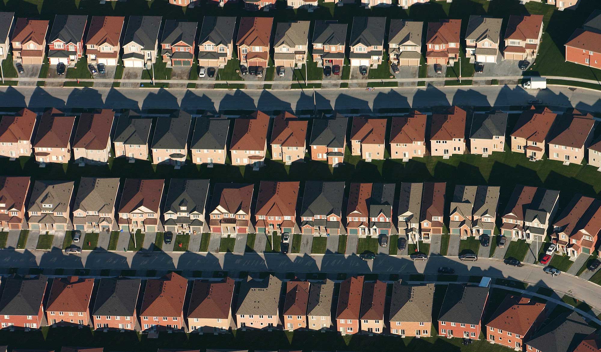 Aerial photograph of a suburb with large houses. The houses have very little space between them. Each house has a small lawn and a driveway in front and lawn in the back.