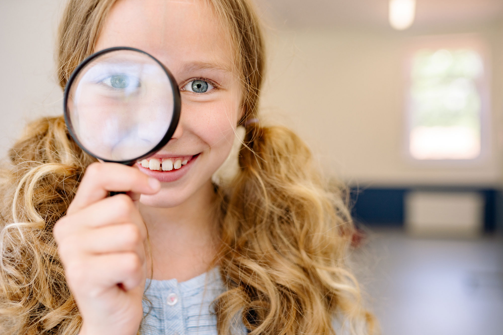 Stock photo of a girl holding a magnifying glass up to her eye.